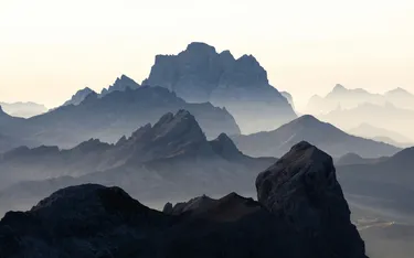 Mehrere Berggipfel in den Dolomiten mit nebligen Tälern und einer lichtdurchfluteten Atmosphäre, typische Landschaft aus Alta Badia, Südtirol.