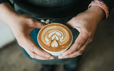 Person hält eine Tasse mit Latte Art Camouflage-Muster, Nahaufnahme, im Vordergrund.