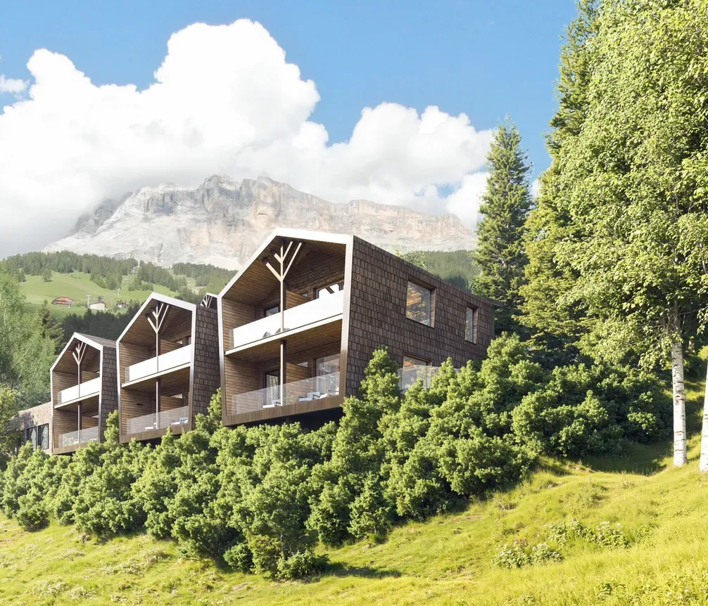 Villetta moderna su pendio verde con balconi di vetro, circondata da alberi e montagne sullo sfondo.