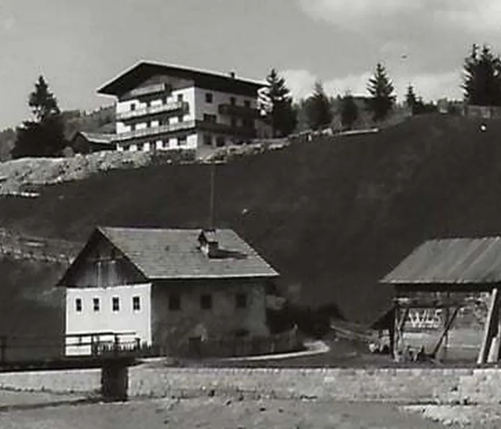 Immagine di un paesaggio montano in bianco e nero nella regione delle Dolomiti, con edifici tradizionali e una moderna struttura in alto sul pendio.