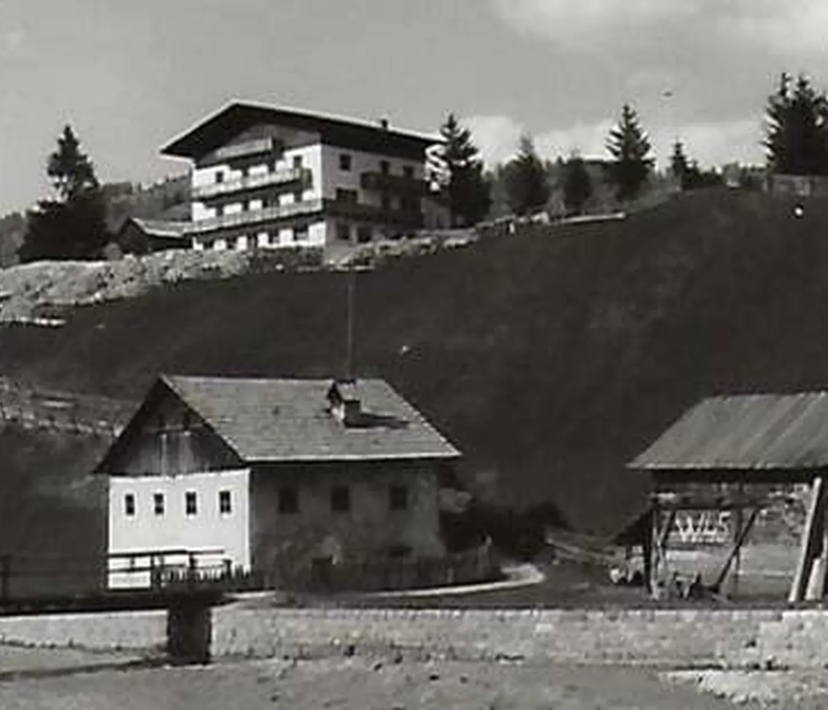 Immagine di un paesaggio montano in bianco e nero nella regione delle Dolomiti, con edifici tradizionali e una moderna struttura in alto sul pendio.