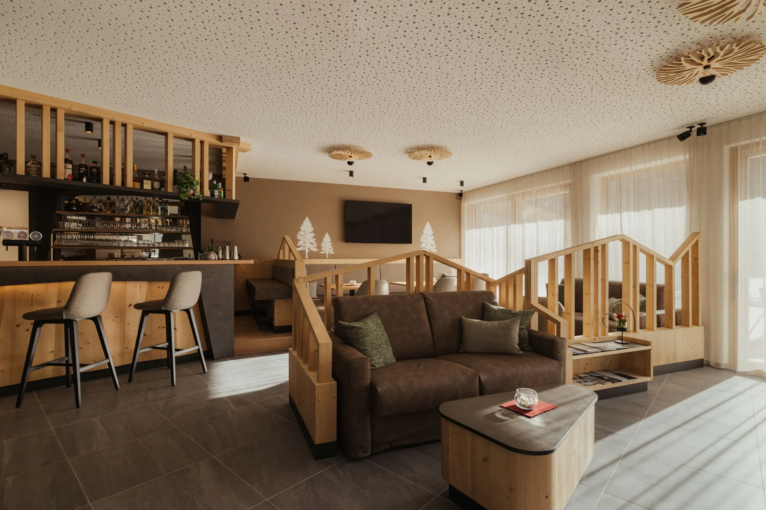 Moderne Lounge mit gemütlichen braunen Sofas, Holzbar und hohen Hockern. Sanfte Beleuchtung, Wald-Wandkunst, große Fenster und eine ruhige Atmosphäre.