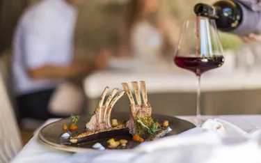 Gegrillte Lammkoteletts mit Gemüse und Rotweinglas auf einem gedeckten Tisch in einem eleganten Restaurant.