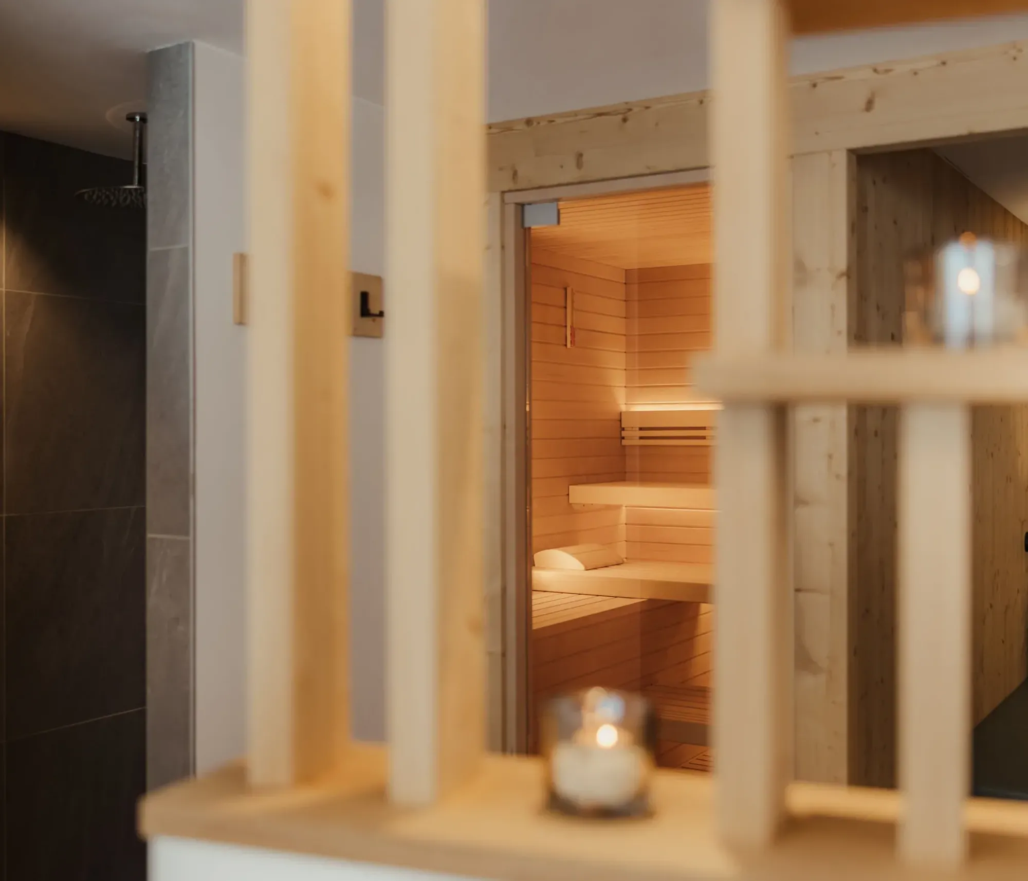 Cozy spa interior featuring a warm-lit wooden sauna room. Soft candlelight flickers on a wooden shelf, creating a serene, relaxing atmosphere.
