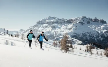 Zwei Skifahrer in Winterkleidung auf einer schneebedeckten Landschaft vor den Dolomiten in Alta Badia, Dolomitenregion.
