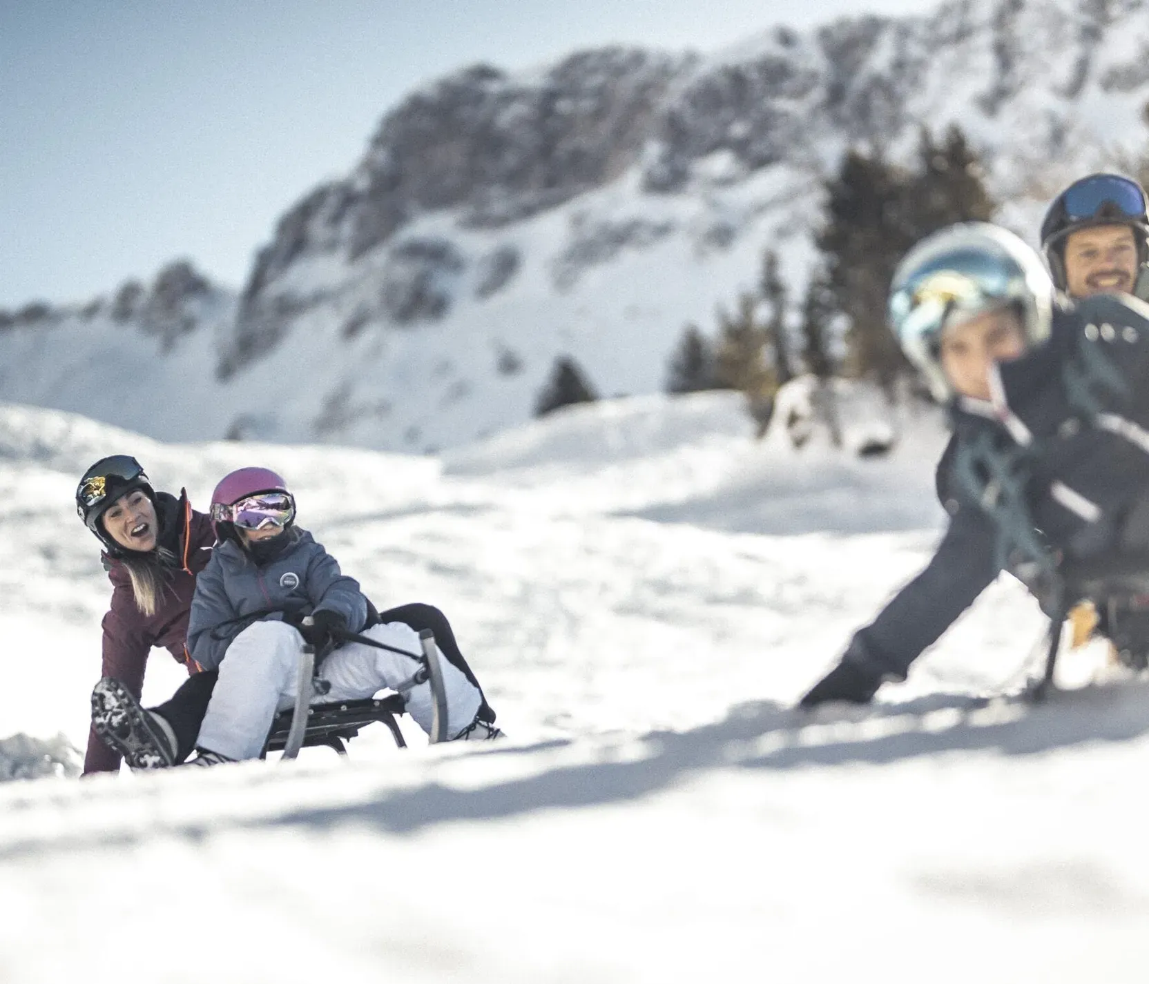 Familie beim Rodeln im Schnee vor Bergen in Alta Badia, Dolomiten, mit lachenden Gesichtern und Winterkleidung.