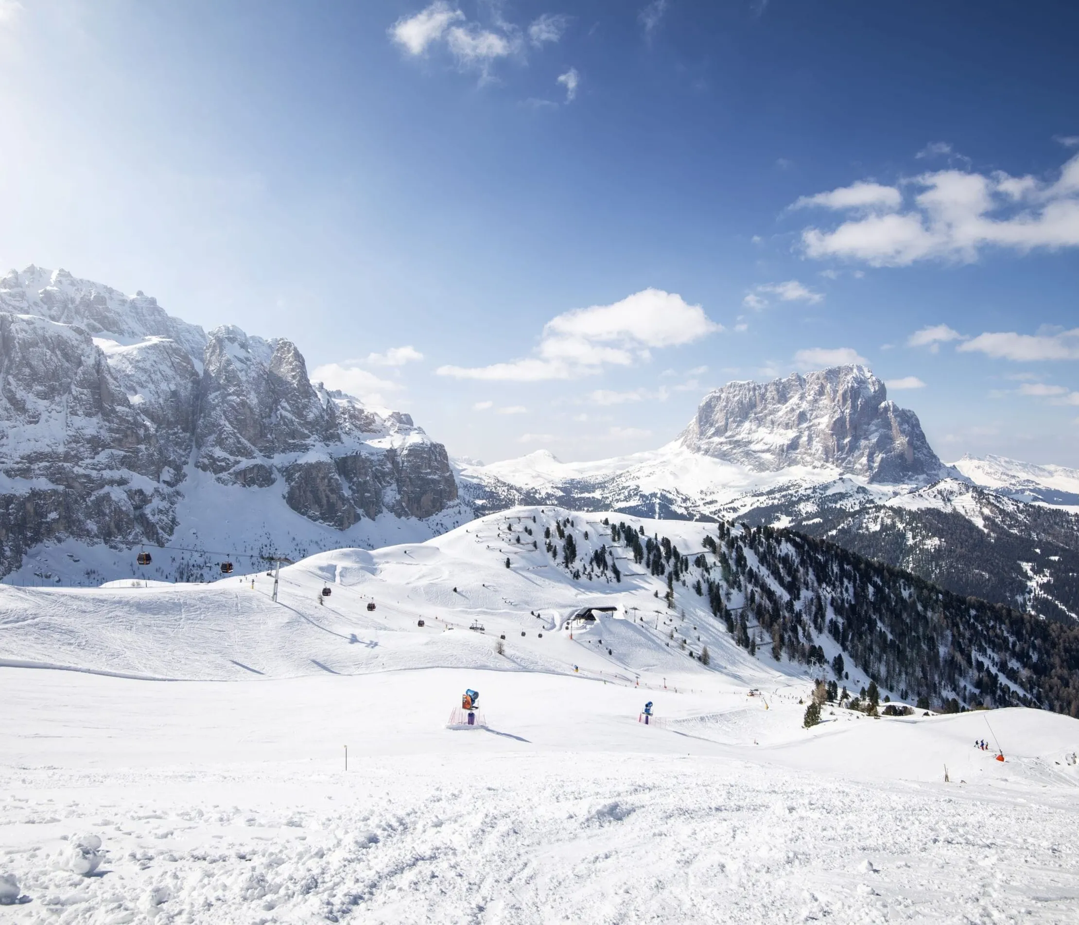 Verschneite Berge und Pisten im Dolomiten-Gebirge bei sonnigem Himmel in Alta Badia, Dolomitenregion, mit Skifahrern und Skiliften.