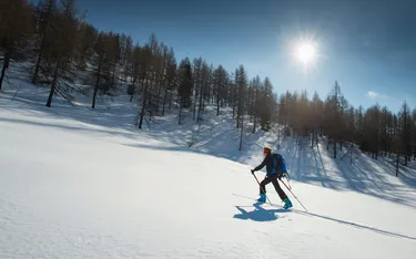 Skifahrer auf steilem, verschneitem Hang in den Dolomiten, Sonne scheint, blauer Himmel, Bäume am Hang, in Alta Badia, Dolomitenregion.