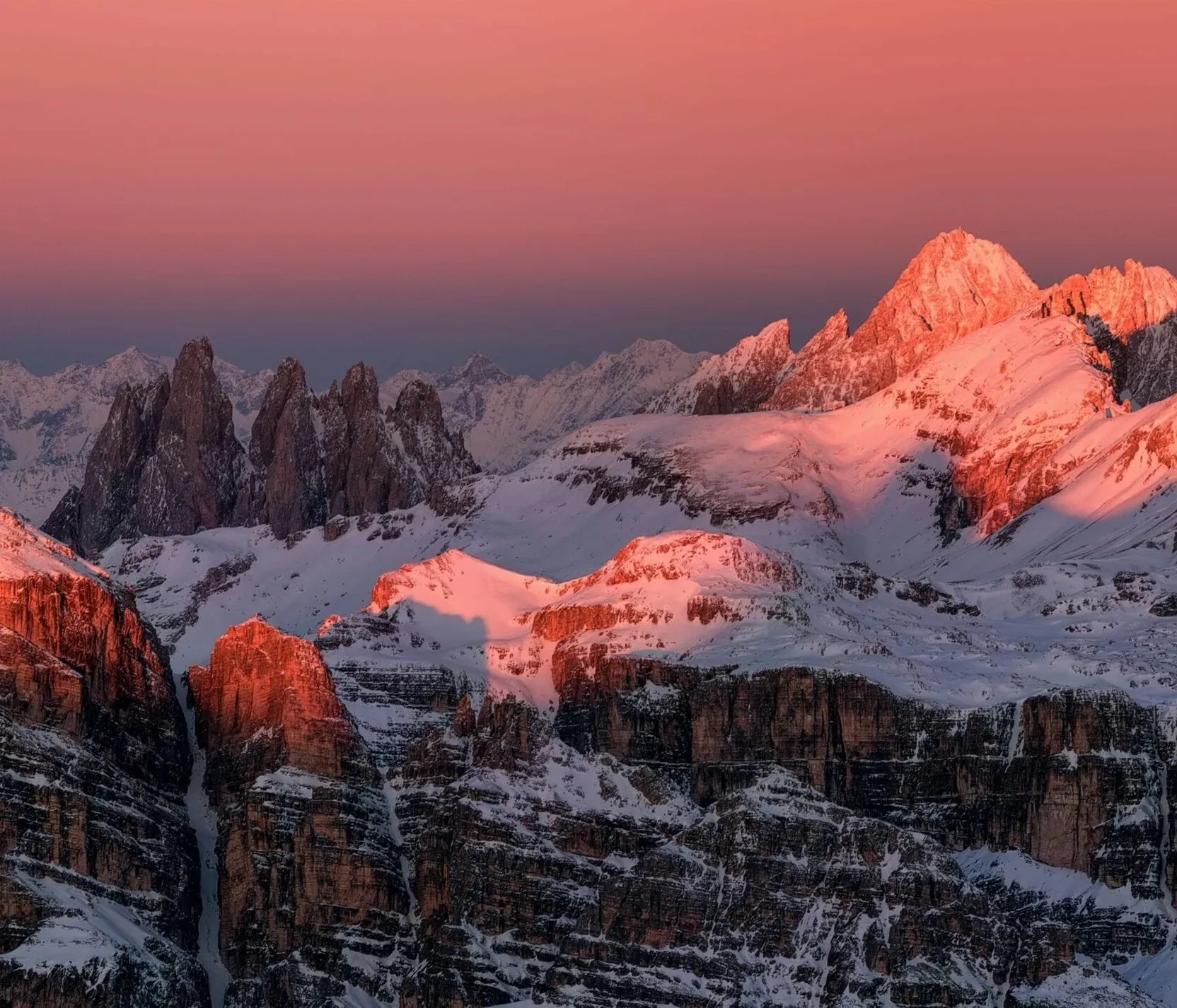 Berggipfel im Sonnenuntergang in den Dolomiten mit schneebedeckten Gipfeln und pink-orangem Himmel.
